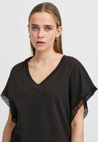 Zwarte V-hals T-shirt van zacht materiaal met korte mouwen, voorzien van intricately zwarte kant trim langs de randen.