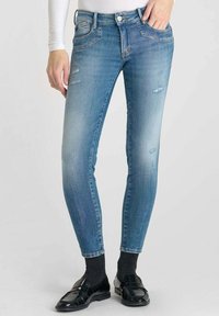 Jean skinny en denim bleu clair, avec des zones décolorées et des détails usés, doté de poches avant et d'une fermeture à bouton classique.