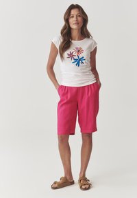 White short-sleeve t-shirt with colorful flower graphic; bright pink knee-length shorts; brown slide sandals. Simple, casual outfit.