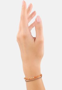 Braccialetto con perline arancioni, piccoli dettagli metallici e un design a catena stratificata, indossato sul polso di una donna con uno sfondo neutro.