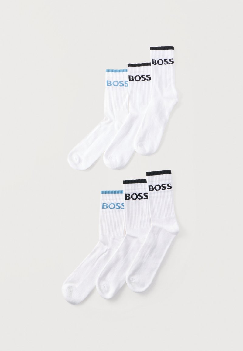 Six chaussettes blanches basses avec des bords côtelés, trois portant « BOSS » en noir, trois avec « BOSS » en bleu clair, disposées sur un fond uni.