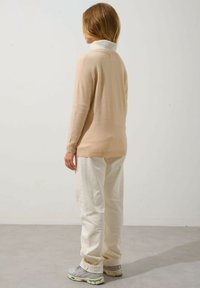 Maglione beige chiaro con colletto a coste alte, dettagli crema e vestibilità comoda. Abbinato a pantaloni rilassati di un bianco sporco e sneakers grigie.
