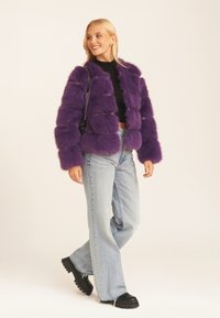 Purple faux fur jacket with a boxy design, featuring a shaggy texture, front clasp, and paired with light blue denim and black chunky boots.