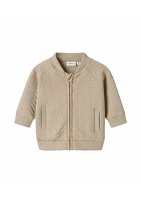 Giacca trapuntata beige con zip frontale, maniche raglan, polsini a costine e colletto rotondo. Presenta tasche laterali e un motivo a zigzag testurizzato.