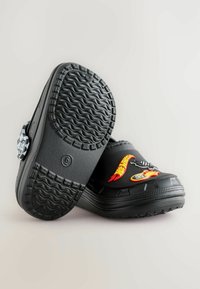 Black clogs with a textured rubber outsole, featuring red, yellow, and white decorative Hot Wheels-themed appliqués and a bold design.