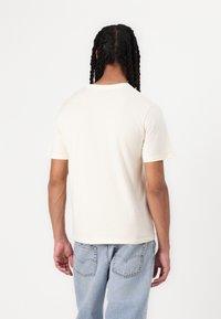 Crème-kleurig katoen T-shirt met korte mouwen, ronde hals en een relaxed fit, van achteren weergegeven tegen een witte achtergrond.