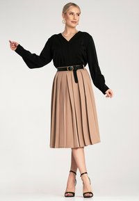 Czarna bluzka z długim rękawem i plisowana beżowa spódnica, ściśnięta czarnym paskiem z złotą klamrą, w połączeniu z czarnymi sandałkami na obcasie.