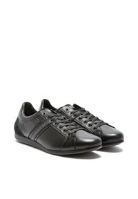 Zapatillas de cuero negro con acentos de ante, punta redondeada, suela plana y diseño con cordones. Presenta detalles de costura y un logotipo en el lateral.