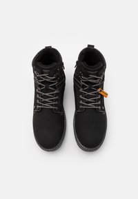 Bottines noires en cuir lisse, dotées de lacets gris, d'une doublure en fourrure texturée et d'une étiquette orange bien visible sur le côté.