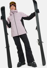 Ski jacket in light purple and black, featuring a zip closure, paired with black ski pants and skis, with orange and black goggles.