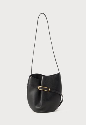 Borsa a secchiello in pelle nera con una lunga tracolla e una cintura orizzontale con una fibbia ovale dorata su sfondo bianco.