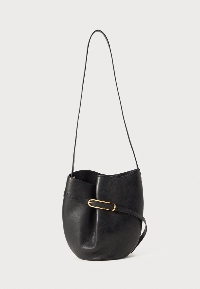 Črna usnjena torba v obliki vedra z dolgim trakom in vodoravno pasom z zlatim ovalnim sponko na belem ozadju.