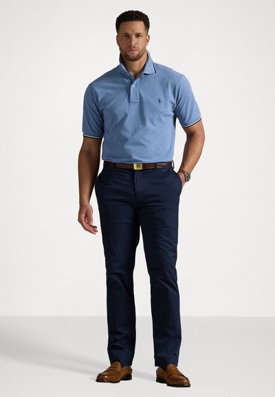 Γαλάζιο πόλο μπλουζάκι με γιακά και ναυτικές λεπτομέρειες, συνδυασμένο με ναυτικές παντελόνες και καφέ loafers. Αξεσουάρ: ασημένιο ρολόι στον καρπό.