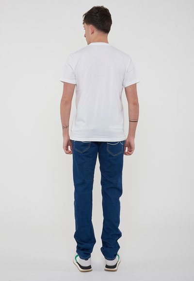 T-shirt bianca in cotone a maniche corte, abbinata a jeans di denim blu. I jeans presentano tasche posteriori con sottili dettagli di cucitura.