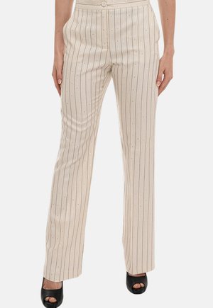 Pantaloni beige a gamba dritta con sottili righe nere verticali e piccoli puntini bianchi, indossati con tacchi neri aperti.