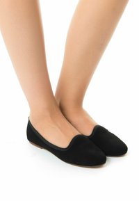 Ballerine in suede nero con una superficie liscia, punta arrotondata e rifiniture elasticizzate, poggiate su una suola in legno chiaro.