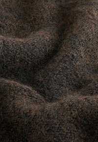 Brunt texturerad tyg med en lurvig yta, med ett vävt mönster. Materialet ser mjukt och varmt ut, med varierande nyanser av brunt.