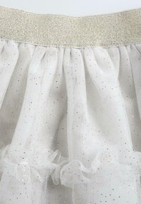 Jupe en tulle blanche avec une taille élastique dorée, ornée d'accents volants et d'un motif éparpillé de points dorés.
