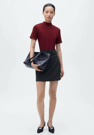 Haut bordeaux à manches courtes, jupe noire ceinturée et grand sac fourre-tout bleu marine. Chaussures noires avec nœuds. Design simple et lignes épurées.