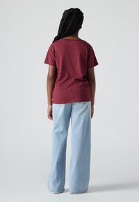 Βουργουνδίζα βαμβακερή μπλούζα με κοντά μανίκια, συνδυασμένη με ανοιχτό μπλε φαρδύ παντελόνι, αναδεικνύοντας μια χαλαρή εφαρμογή και απλό σχέδιο.