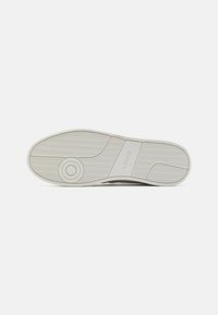 Białe sneakersy z teksturowaną gumową podeszwą, okrągłymi wzorami i wytłoczonym logo. Podeszwa zewnętrzna ma wzór fali, który zapewnia przyczepność.