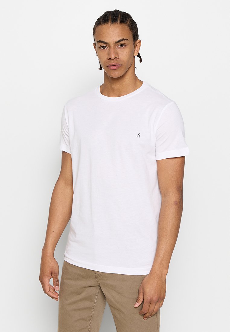 Camiseta blanca de algodón con mangas cortas y escote redondo. Presenta un pequeño logo negro bordado en el lado izquierdo del pecho. Ajuste casual.