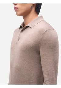 Tan långärmad pikétröja med mjuk struktur, klassisk krage och knapplist med två knappar, som har en figurnära silhuett.