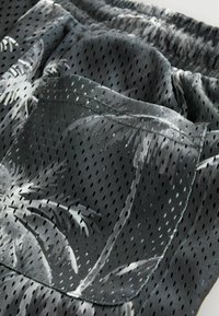 Pantaloni corti in mesh neri e grigi con stampa di palme, vita elasticizzata e una singola tasca posteriore con bordo cucito.