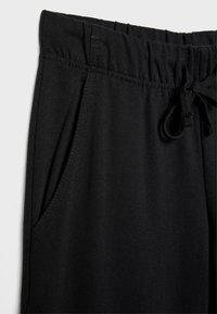 Schwarze Jogginghosen mit einer lockeren Passform, elastischem Bund, Kordelzugverschluss und seitlichen Taschen mit sichtbaren Nähdetails.