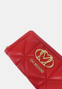 Portafoglio trapuntato rosso in pelle sintetica con logo dorato Love Moschino e chiusura con zip. Caratteristico motivo triangolare all'esterno.