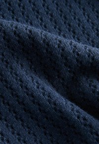 Țesătură tricotată albastru marin cu un model texturat de diamante mici, având o suprafață moale și pufoasă și fibre de ață vizibile pe toată suprafața.