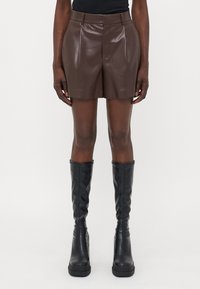 Shorts en simili cuir marron avec une texture lisse, dotés d'une taille haute, de plis et d'une coupe ajustée. Associés à des bottes noires montantes.