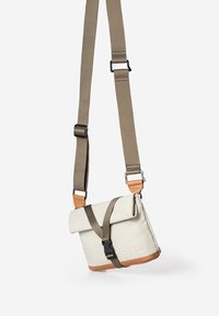 Kleine schoudertas in beige canvas met een gevouwen bovenkant, een bruine leren bodem en een verstelbare kaki-riem. Heeft een gesp sluiting.