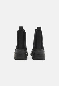 Sorte ankel støvler med ruskind og elastiske paneler, med en tyk gummisål og trækflapper bagpå. Guld "GANT"-logo på hælområdet.