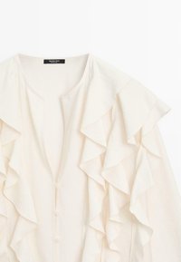 Crème blouse met gerimpelde mouwen en een V-hals. Gemaakt van lichte stof, met een knoopsluiting langs het middenvoorkant.