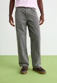 Gray wide-leg pants made of denim with visible seam details. Paired with brown and black hiking shoes, standing on green flooring.