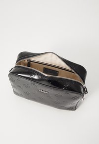 Borsa in vernice nera con chiusura a zip, motivo logo in rilievo e interno beige. Presenta bordi eleganti e dettagli in hardware color argento.