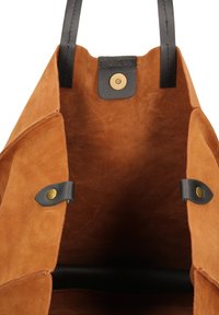 Suède tote bag in bruin met zwarte leren accenten. Heeft een afgeronde bovenkant, magnetische drukknoopsluiting en een binnenvak. Zachte textuur.