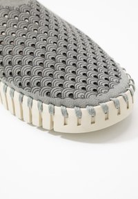 Scarpa grigia lavorata a maglia con un motivo ondulato, suola in gomma beige e dettagli di cucitura in rilievo. Il design presenta una parte superiore flessibile e testurizzata.