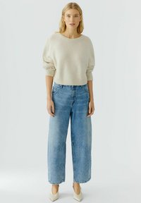 Crème, chunky gebreide trui met een ronde halslijn, gecombineerd met blauwe, wijde denim jeans. Vierkante hakken compleet de outfit.