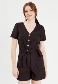 Combinaison short noire avec un décolleté en V, des manches courtes, quatre boutons sur le devant et une taille ceinturée. Tissus lisse avec une silhouette ajustée.