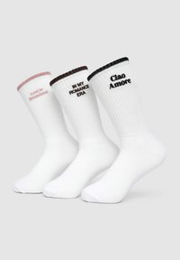 Trzy pary białych skarpetek z prążkowanymi mankietami. Każda z innym napisem: różowa "Zagubiona w Krainie Marzeń", brązowa "W MOJEJ ERZE ROMANSU" oraz czarna "Ciao Amore."