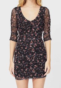 Robe noire à motifs floraux avec manches longues transparentes, comportant un décolleté en V, une texture froncée et de petits motifs floraux multicolores sur toute la surface.