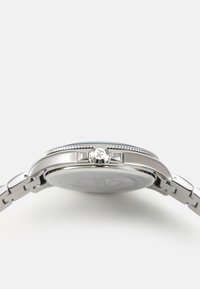 Orologio in acciaio inossidabile argentato con cassa rotonda, lunetta testurizzata e bracciale a maglie argentate. Presenta una corona sul lato per la regolazione.
