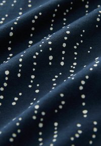 Marinblått tyg med en texturerad yta, prydd med spridda vita prickar av varierande storlek i ett vertikalt mönster.