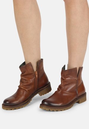 Bottines en cuir marron au design décontracté, présentant une fermeture éclair sur le côté, une semelle texturée et des détails froncés sur le dessus.