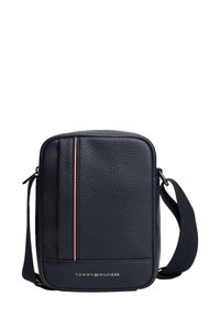 Laivastonsininen nahkainen olkalaukku, jossa on kupruileva pinta, pystysuora punavalkoinen raita, säädettävä olkahihna ja kullanvärinen logo alareunassa.