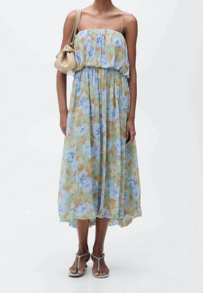 Blumen-Maxikleid in Grün-, Blau- und Orangetönen, mit gerafftem Oberteil und verstellbaren Spaghettiträgern. Kombiniert mit einer cremefarbenen Handtasche.