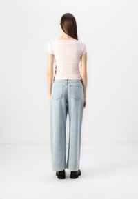 Vaaleanpunainen istuva ribbipaita yhdistettynä löysiin vaaleansinihin farkkuihin. Farkuissa on klassinen viiden taskun muotoilu ja käännetyt lahkeet. Mustat saappaat näkyvät.