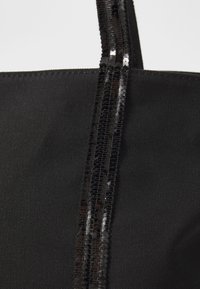 Sac fourre-tout noir avec une texture de tissu lisse, orné de deux rangées verticales de sequins noirs brillants.